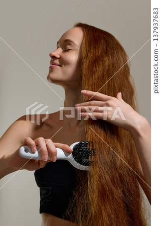 Woman brushing long hair with paddle brush in studio. 137937683