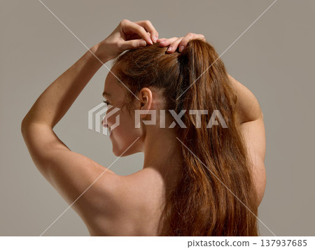 Woman tying long hair into ponytail in studio. 137937685