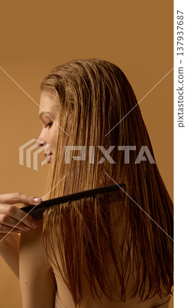 Woman combing wet hair with black comb on warm background. 137937687