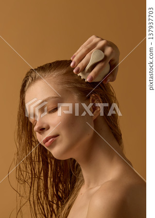 Woman massaging scalp with brush during hair care routine. 137937703