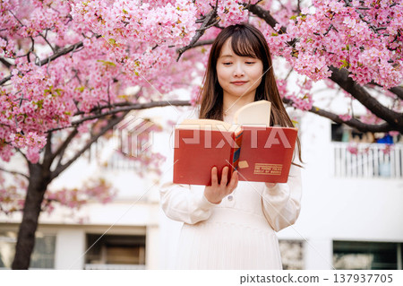 A young woman reading in front of a cherry tree A young woman reading in front of a cherry tree 137937705