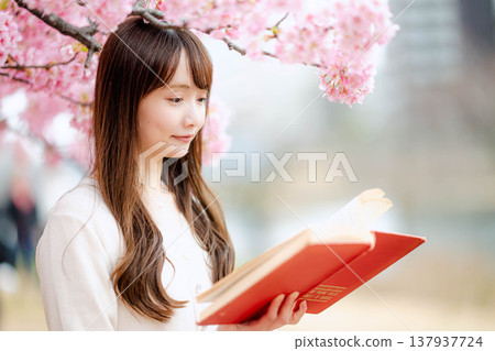 A young woman reading in front of a cherry tree A young woman reading in front of a cherry tree 137937724