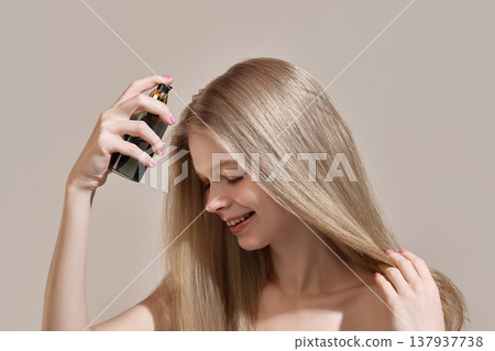 Woman spraying cosmetic product onto long blonde hair in studio setting. 137937738
