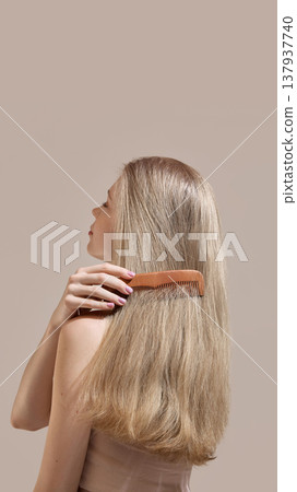 Woman brushing long smooth blonde hair with wooden comb on neutral background. Woman brushing long smooth blonde hair with wooden comb on neutral background. 137937740
