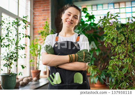 Running of own business. Young woman florist wearing apron in botanical store with green plants. Happy small business owner working at flower shop standing surrounded by plants. Small business 137938118