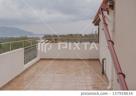 A broken rain pipe hanging at an awkward angle on a modern terrace. Detached from the gutter due to poor installation, it serves as a clear example of drainage failure 137938634