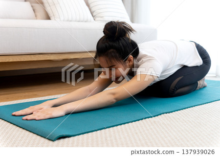 young woman is stretching out on a yoga mat in a sitting forward fold position young woman is stretching out on a yoga mat in a sitting forward fold position 137939026