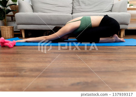 young woman do yoga near sofa in living room in her house in pose Paschimottanasana young woman do yoga near sofa in living room in her house in pose Paschimottanasana 137939317