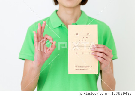 A middle-aged female care worker makes a circular pose while holding her pay envelope. A middle-aged female care worker makes a circular pose while holding her pay envelope. 137939483