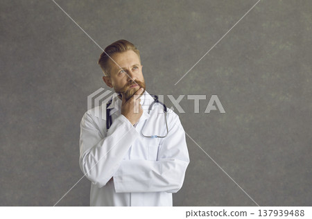 Portrait of a serious male doctor with a pensive expression on a gray background. Portrait of a serious male doctor with a pensive expression on a gray background. 137939488
