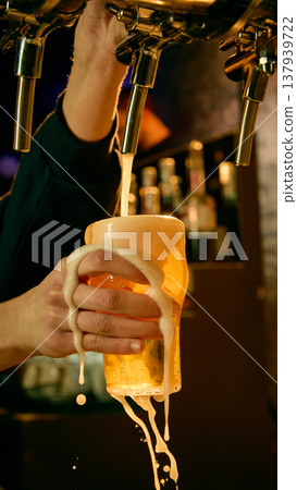Draft beer pouring into glass with foam spilling over bartender hand in bar. Draft beer pouring into glass with foam spilling over bartender hand in bar. 137939722