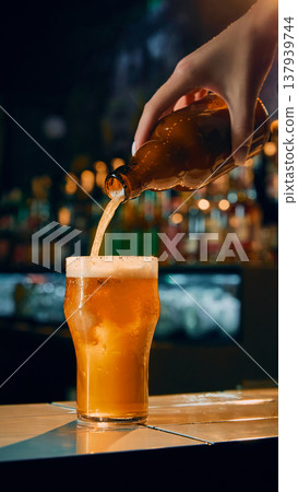Beer being poured from bottle into glass on bar counter with foam forming. Beer being poured from bottle into glass on bar counter with foam forming. 137939744