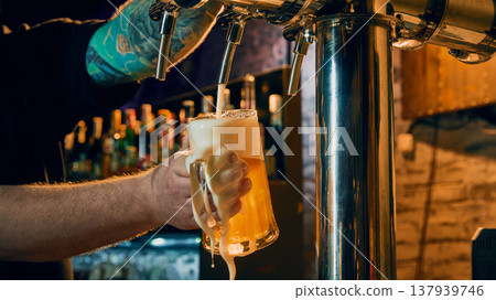Bartender pouring draft beer into glass mug with foam dripping in bar close up 137939746