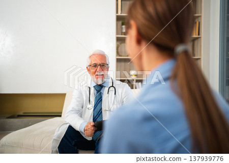 Senior man doctor examining young woman in doctor office clinic or at home. Girl patient and doctor have consultation in hospital room. Medicine healthcare medical checkup. Visit to doctor Senior man doctor examining young woman in doctor office clinic or at home. Girl patient and doctor have consultation in hospital room. Medicine healthcare medical checkup. Visit to doctor 137939776