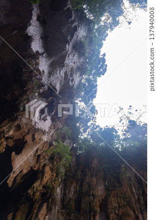 Upward view from inside Batu Caves near Kuala Lumpur, Malaysia. Showing a natural opening in the limestone cave with sunlight and greenery. Upward view from inside Batu Caves near Kuala Lumpur, Malaysia. Showing a natural opening in the limestone cave with sunlight and greenery. 137940008