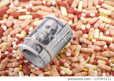 Hundred dollar bills banknotes on heap of colorful medicine pills or dietary supplements. Medical costs concept. Hundred dollar bills banknotes on heap of colorful medicine pills or dietary supplements. Medical costs concept. 137941211