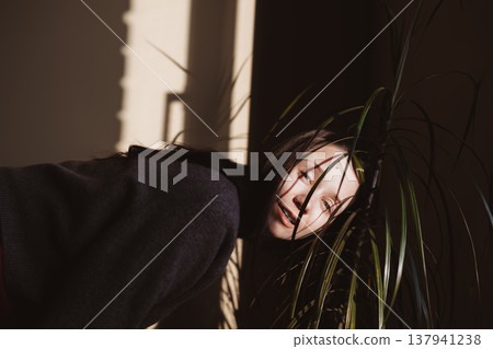 Moody cinematic portrait of a woman looking through green palm leaves. Creative shadow play, authentic emotion, and hard sunlight indoors. Moody cinematic portrait of a woman looking through green palm leaves. Creative shadow play, authentic emotion, and hard sunlight indoors. 137941238