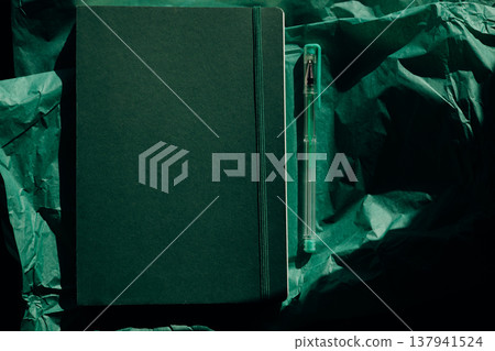 Dark green notebook with elastic band and transparent pen on wrinkled tissue paper. Minimalist stationery aesthetic flat lay, monochrome background Dark green notebook with elastic band and transparent pen on wrinkled tissue paper. Minimalist stationery aesthetic flat lay, monochrome background 137941524
