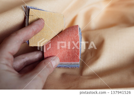 Close-up of hand flipping through colorful fabric swatches on linen background. Sustainable fashion design, textile selection, eco-friendly materials Close-up of hand flipping through colorful fabric swatches on linen background. Sustainable fashion design, textile selection, eco-friendly materials 137941526