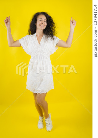Woman dancing happily celebrating success on yellow background Woman dancing happily celebrating success on yellow background 137941714