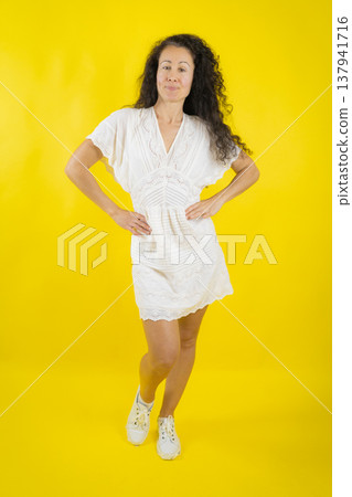 Confident woman posing in white dress on yellow background 137941716