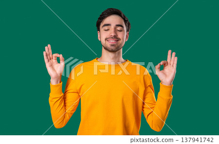Calm Young Guy Relaxing, Meditating, Refuses Stress. Breathes Deeply On Green Calm Young Guy Relaxing, Meditating, Refuses Stress. Breathes Deeply On Green 137941742