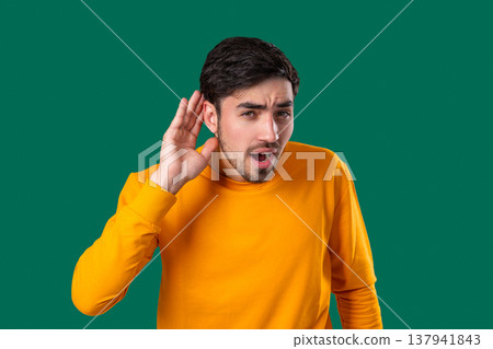 Young Man Pointing To Ear With Confused Face, Signaling He Cant Hear Clearly 137941843