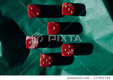 Red marble dice with gold heart pips on green crumpled paper. Romantic gambling concept, Valentine's Day luck, high contrast shadows art photography. 137942389