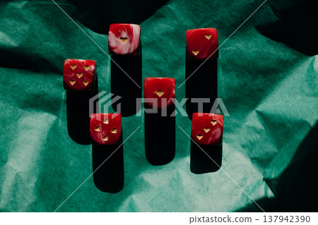 Red marble dice with gold heart pips on green crumpled paper. Romantic gambling concept, Valentine's Day luck, high contrast shadows art photography. 137942390