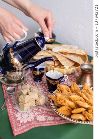 Hands pouring oriental coffee from a carafe into a cup. Baklava close-up. Sweet food. Dessert from dough 137942721