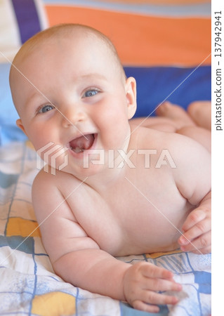 Baby Smiling Joyfully on a Colorful Bedspread 137942941