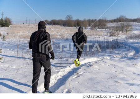 Couple in black gear run on snowy path in open field. Couple in black gear run on snowy path in open field. 137942969