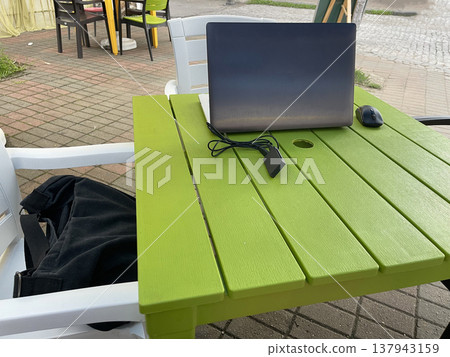 Person working on a laptop at a bright green table in a casual outdoor setting near a city street Person working on a laptop at a bright green table in a casual outdoor setting near a city street 137943159