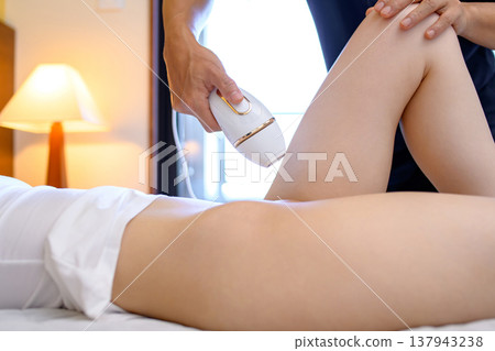 一位女士在伴侶(男友、丈夫)的幫助下使用家用除毛儀進行 VIO 除毛;側視圖。 一位女士在伴侶(男友、丈夫)的幫助下使用家用除毛儀進行 VIO 除毛;側視圖。 137943238