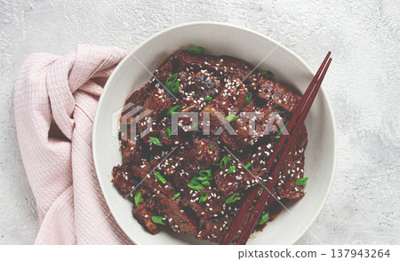 Crispy beef, with green onions and sesame seeds, in a bowl with chopsticks, on a textured surface, on a light background, no people Crispy beef, with green onions and sesame seeds, in a bowl with chopsticks, on a textured surface, on a light background, no people 137943264