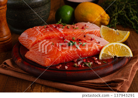 Fresh salmon fillets on a wooden platter with citrus slices and herbs arranged for cooking 137943291