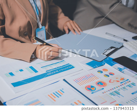 Business colleagues analyzing financial charts and reports on the table while having a focused discussion about strategies and market performance during an important meeting in a modern office setup 137943313