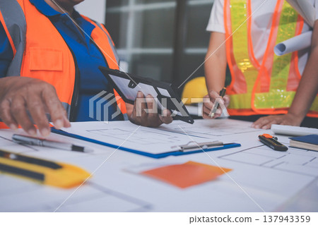 engineer and an architect reviewing blueprints and construction plans together at a bustling construction site engineer and an architect reviewing blueprints and construction plans together at a bustling construction site 137943359