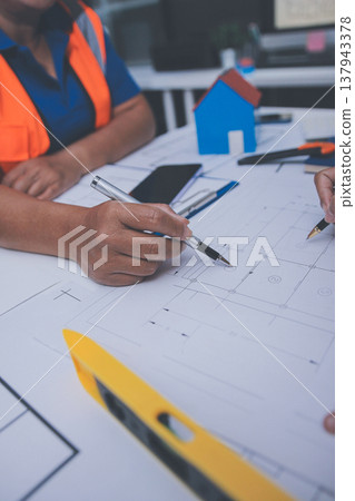 engineer and an architect reviewing blueprints and construction plans together at a bustling construction site 137943378