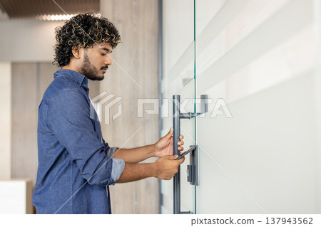 An Indian young man opens the door of an office building using a phone app. An Indian young man opens the door of an office building using a phone app. 137943562