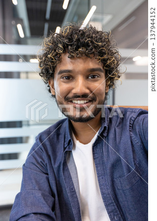 A vertical close-up photo of an Indian man indoors talking to a camera he is holding in his hand. 137944152