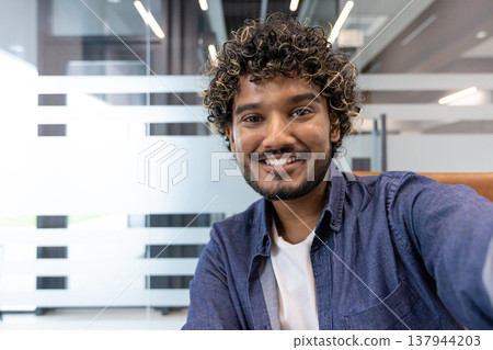 Close-up photo of a young Indian man in an office, talking and looking at the camera. 137944203