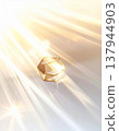 Glowing Faceted Golden Crystal on White Surface with Streaks of Light 137944903
