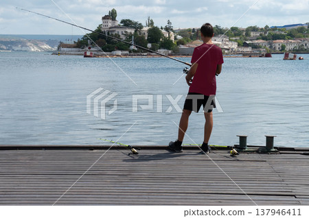 A man stands on a pier by the water, fishing. A man stands on a pier by the water, fishing. 137946411