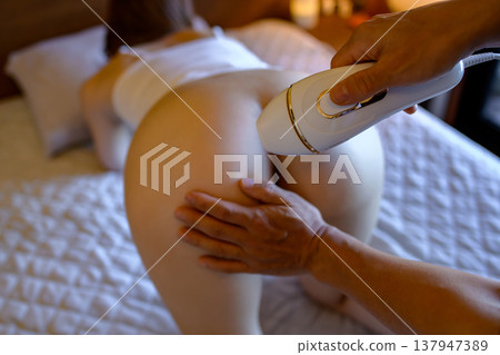 A woman gets help from her partner (boyfriend, husband) with VIO hair removal; on all fours; using a home hair removal device; dim lighting. A woman gets help from her partner (boyfriend, husband) with VIO hair removal; on all fours; using a home hair removal device; dim lighting. 137947389