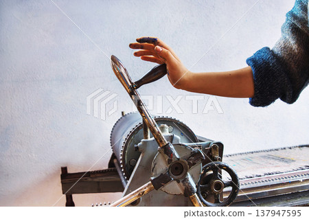 Artist hand operating manual printing press in traditional print studio. Printmaker ink stained hand turning the crank handle 137947595
