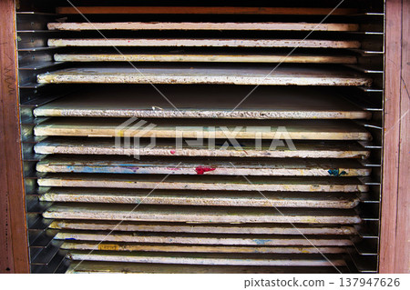 A closeup of wooden drying racks with evenly spaced horizontal trays, holding stacked boards with paper or artworks in a school art classroom. A closeup of wooden drying racks with evenly spaced horizontal trays, holding stacked boards with paper or artworks in a school art classroom. 137947626