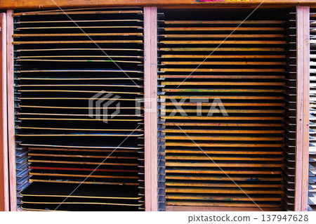 A closeup of wooden drying racks filled with stacked artwork and drawing boards in a studio setting. labeled storage compartments A closeup of wooden drying racks filled with stacked artwork and drawing boards in a studio setting. labeled storage compartments 137947628