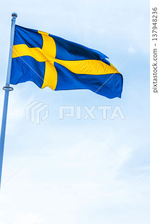 The national flag of Sweden waving on a pole against a clear blue sky. 137948236