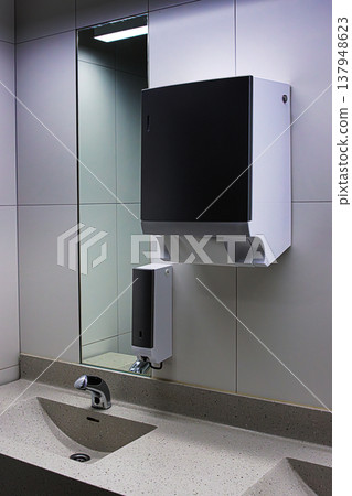 Interior of a modern public restroom with sink, chrome automatic faucet, mirror, soap and towel dispensers. Interior of a modern public restroom with sink, chrome automatic faucet, mirror, soap and towel dispensers. 137948623